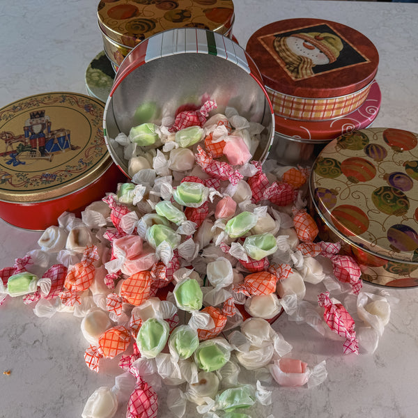 Colorful taffy candies spilling out of decorative tins on a white surface